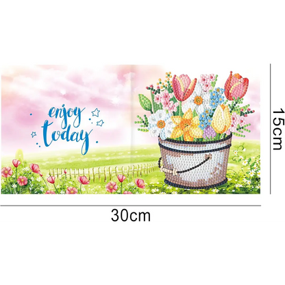 Diamond painting wenskaart met de tekst 'Enjoy today' en een emmer met kleurrijke bloemen tegen een groene achtergrond.